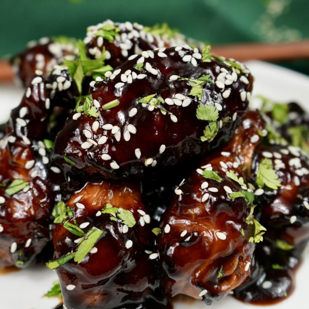 A plate of Hoisin Glazed Chicken Wings garnished with sesame seeds and chopped coriander.