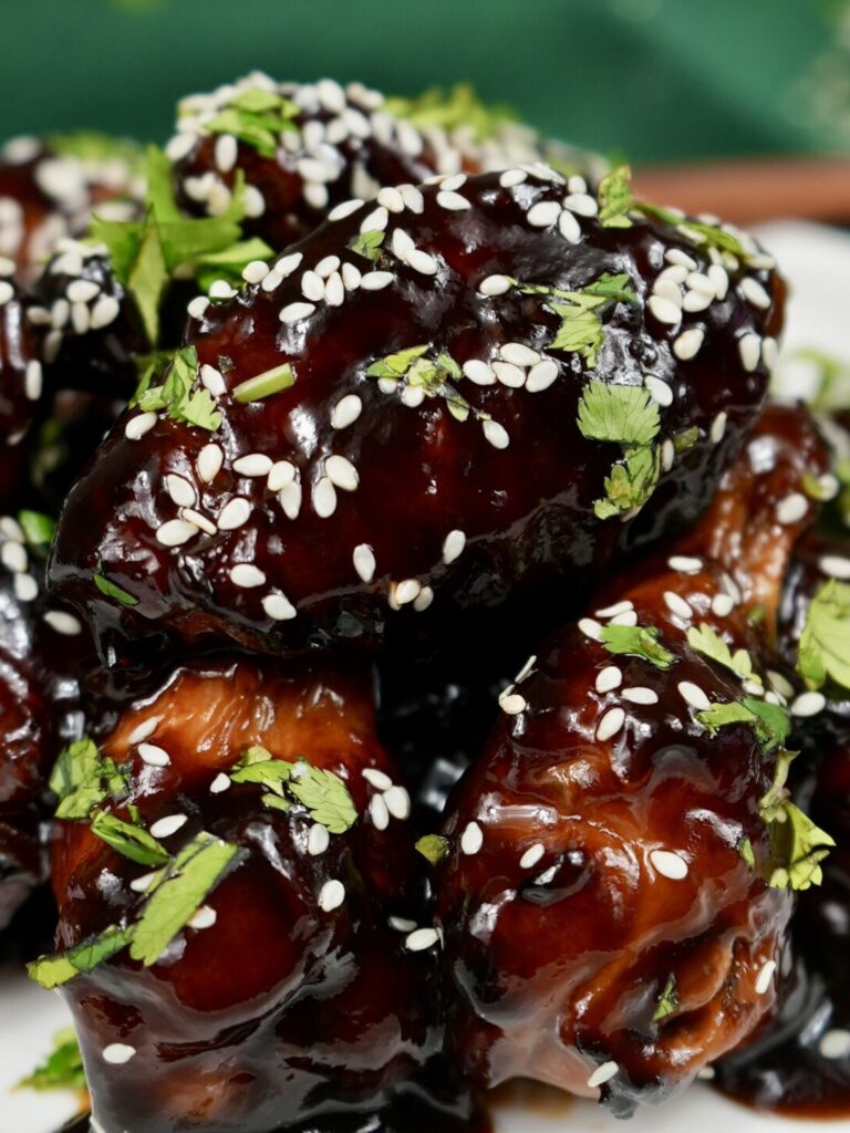 A plate of Hoisin Glazed Chicken Wings garnished with sesame seeds and chopped coriander.