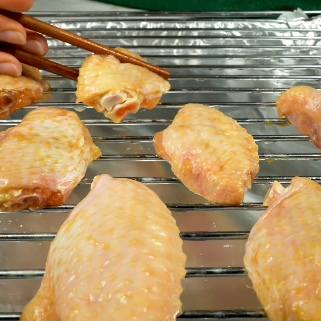 Marinated chicken wings arranged on a greased roasting rack.