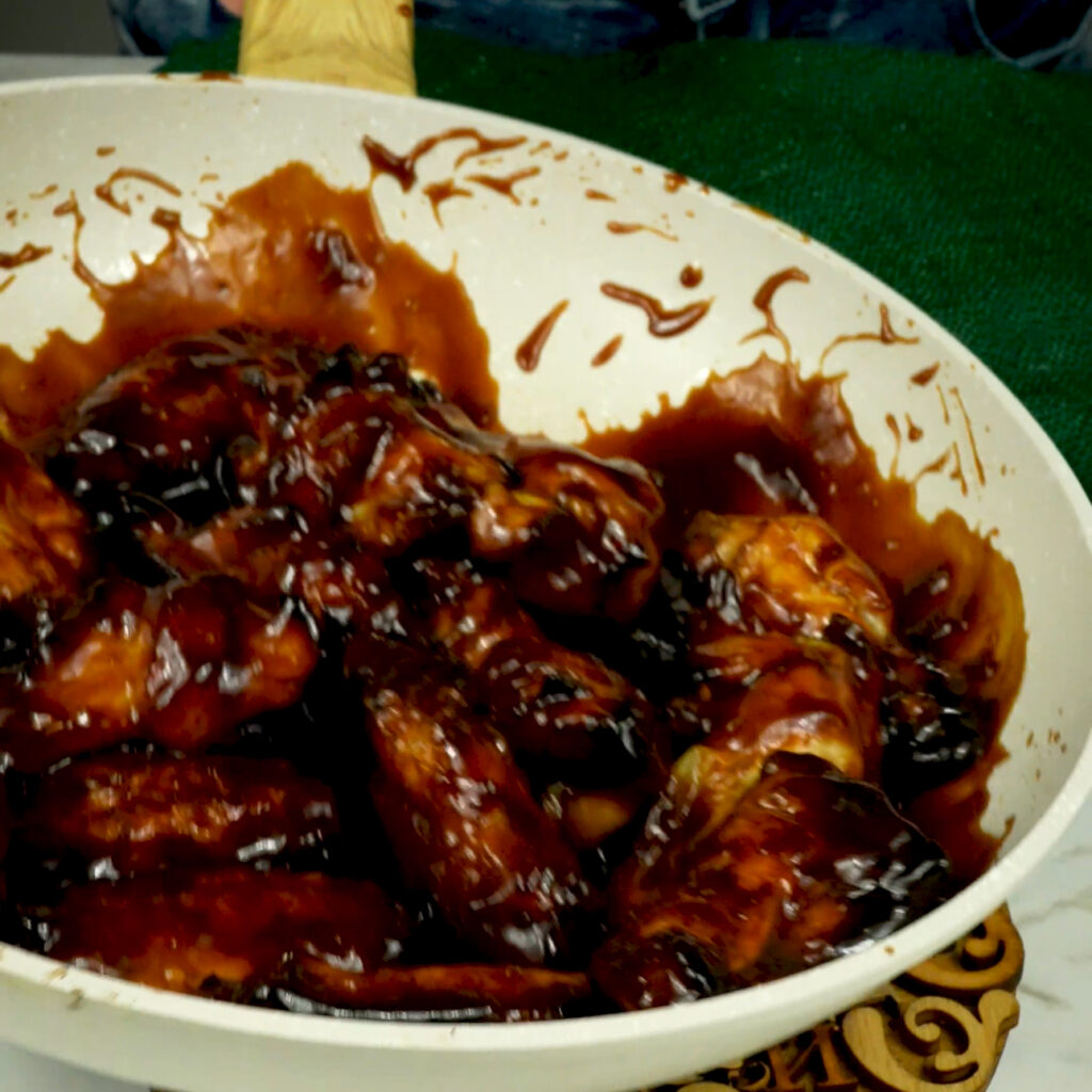 Chicken wings being tossed in hoisin sauce in a frying pan.