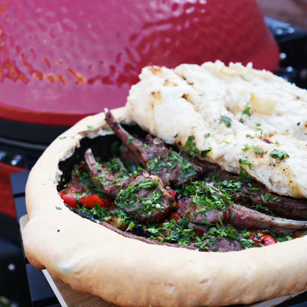 Grilled lamb chops and vegetables enclosed in golden-brown savoury dough, served in a cast-iron skillet.