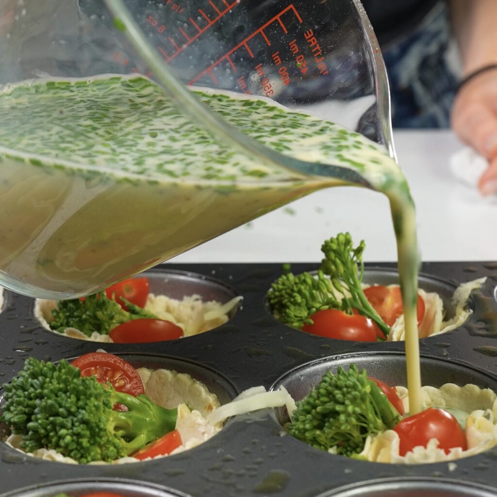 Egg mixture being poured into tortilla cups filled with vegetables.