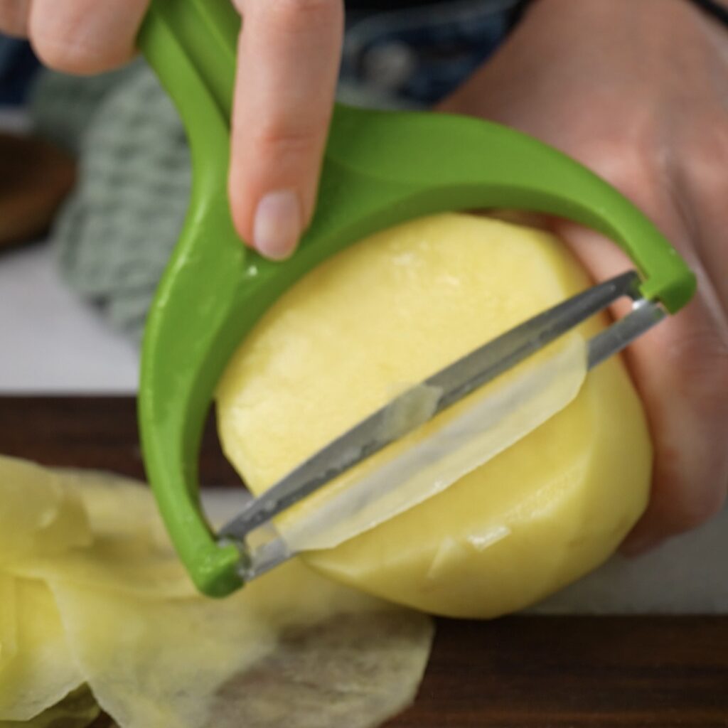 Slicing a potato into thin slices with a vegetable peeler.