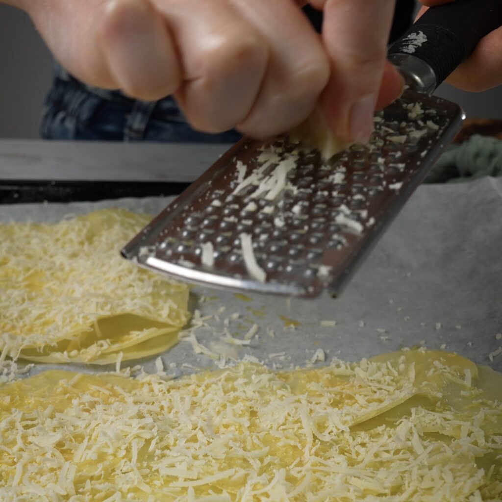 Grating parmesan cheese over potato slices.