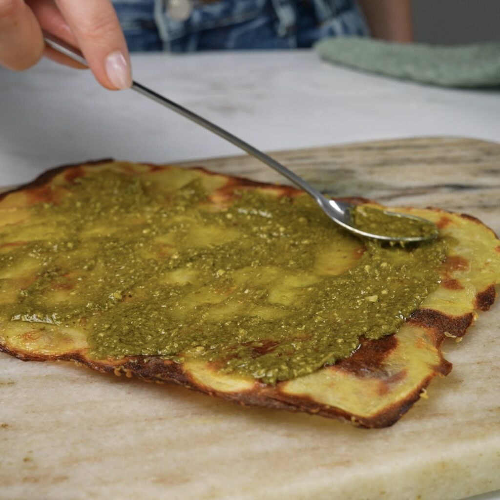 Spreading pesto over a crispy, baked potato slice sheet.