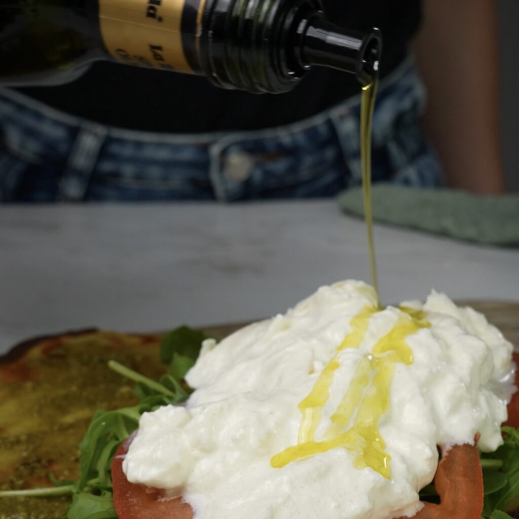 Drizzling olive oil over a creamy burrata cheese.