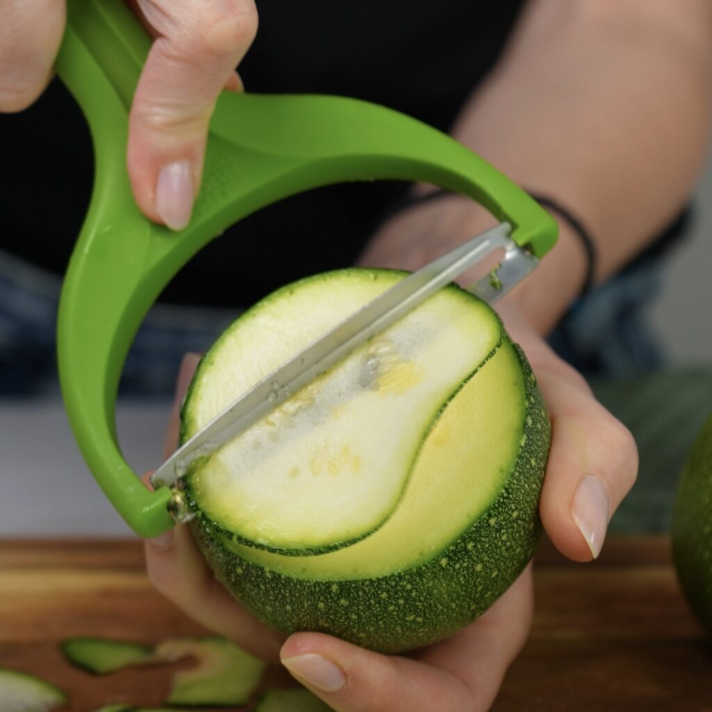 Thin slices of courgette being cut with a vegetable peeler