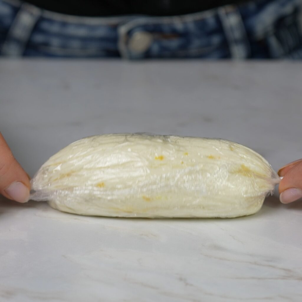 Wrapping a ricotta log tightly with cling film to form an oval shape.