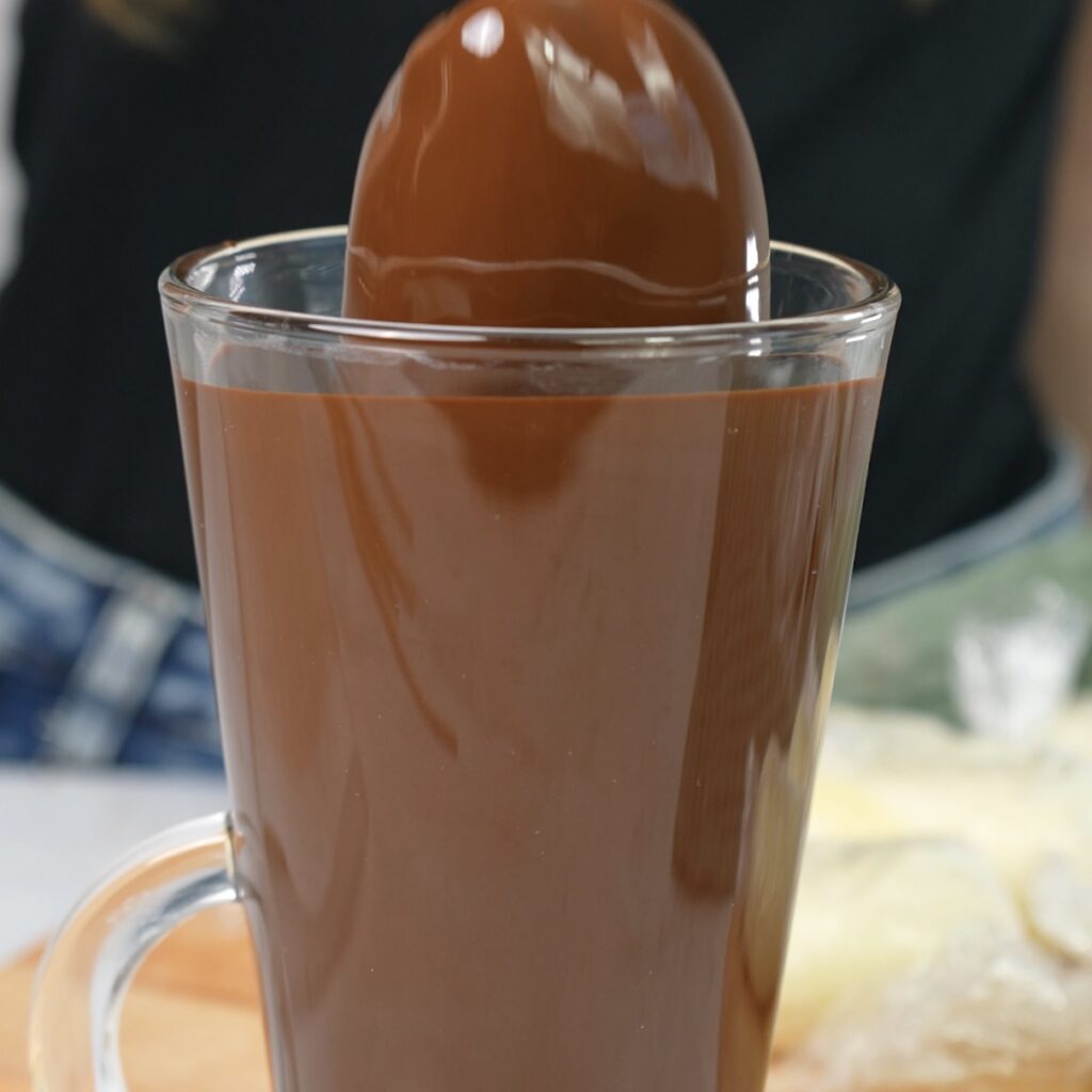 Dipping a ricotta log into a glass of chocolate glaze.