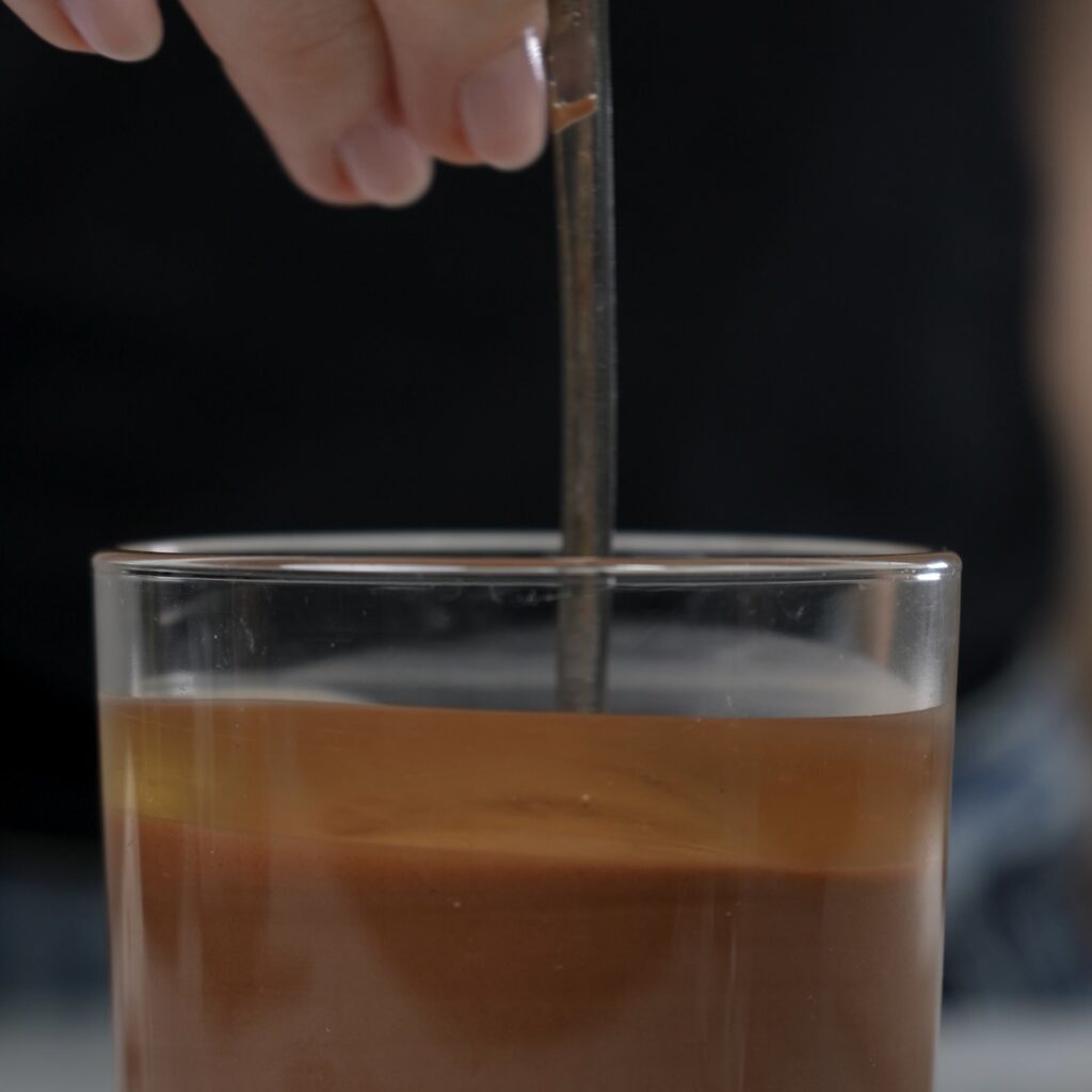 Melted chocolate is mixed with oil in a glass.