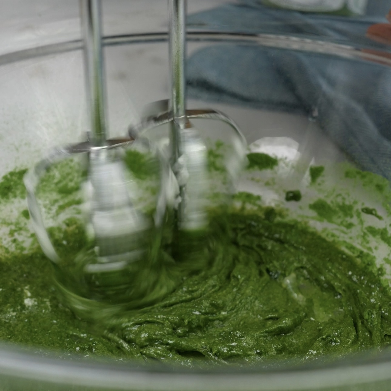 Spinach powder being whisked into egg yolks in a mixing bowl.