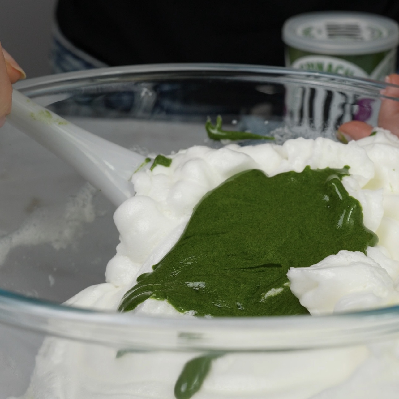 Spinach egg yolk mixture being gently folded into whipped egg whites.