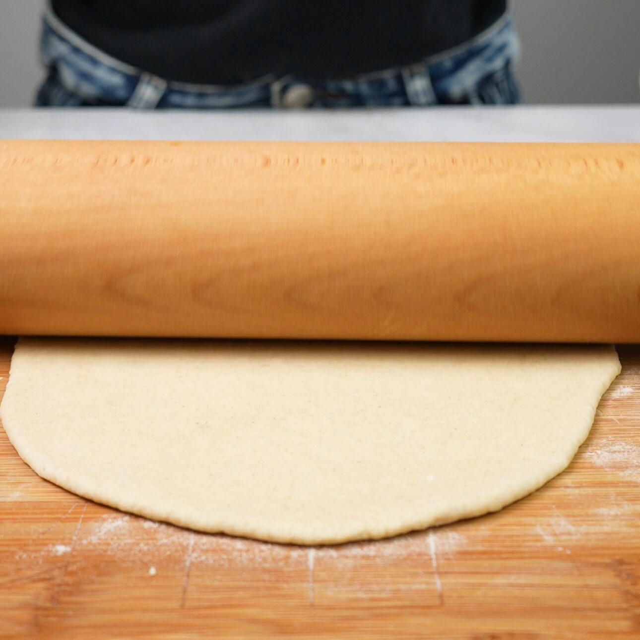 Dough being rolled out with a rolling pin on a floured surface.