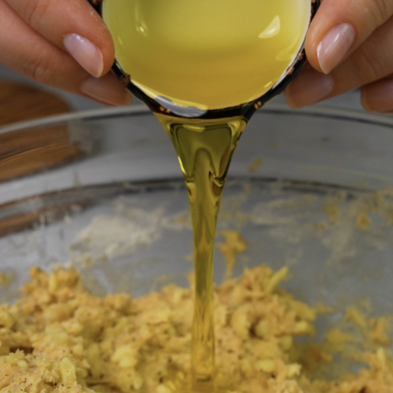 Pouring olive oil into a mixing bowl with dough ingredients.