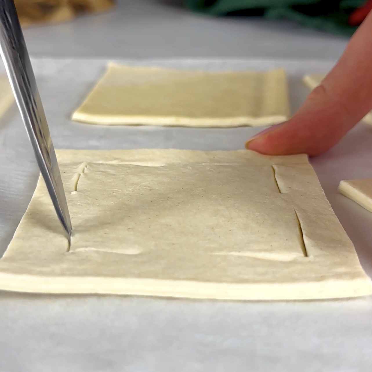 Scoring a 1 cm border inside each puff pastry square, cutting just the corners.