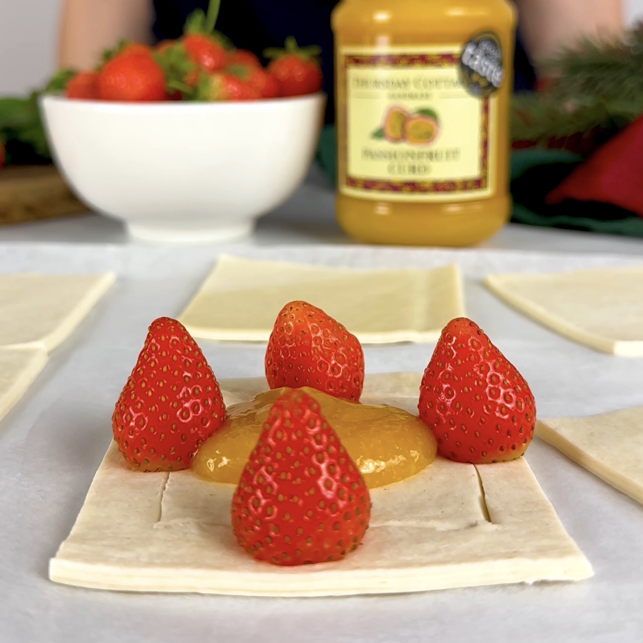 Placing 1 tsp of passion fruit curd in the centre of each puff pastry square and adding a small strawberry