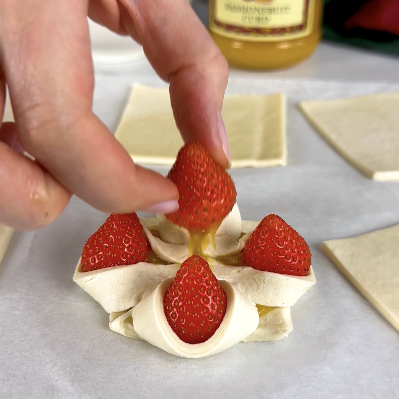 Placing another strawberry on top of the folded puff pastry and pressing gently to seal.