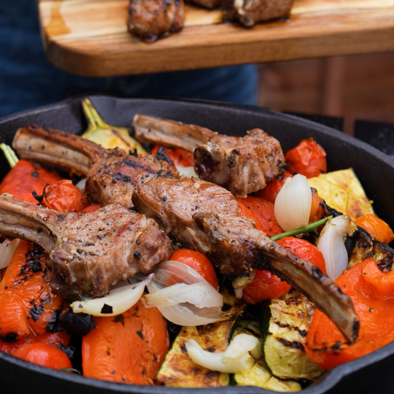 Grilled lamb chops and assorted vegetables arranged in a cast-iron skillet, ready for the next step of cooking.