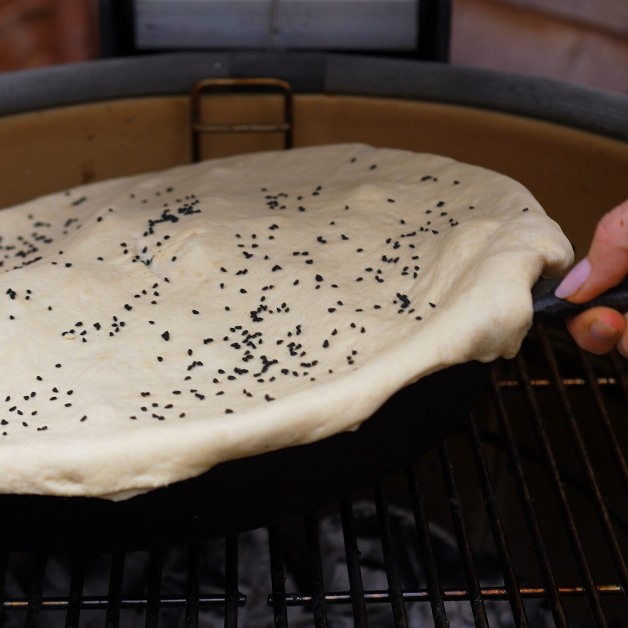 Cast-iron skillet with dough-covered lamb and vegetables placed on the grill