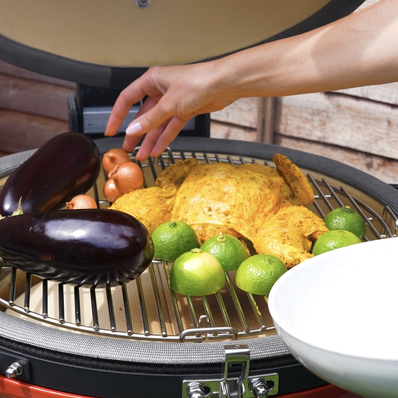 Placing chicken, aubergines, and lime halves on the grill.