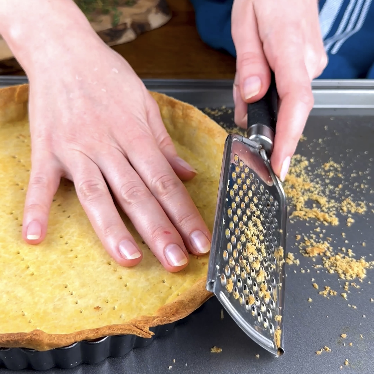 A photo of excess pastry edges being grated off a tart case.