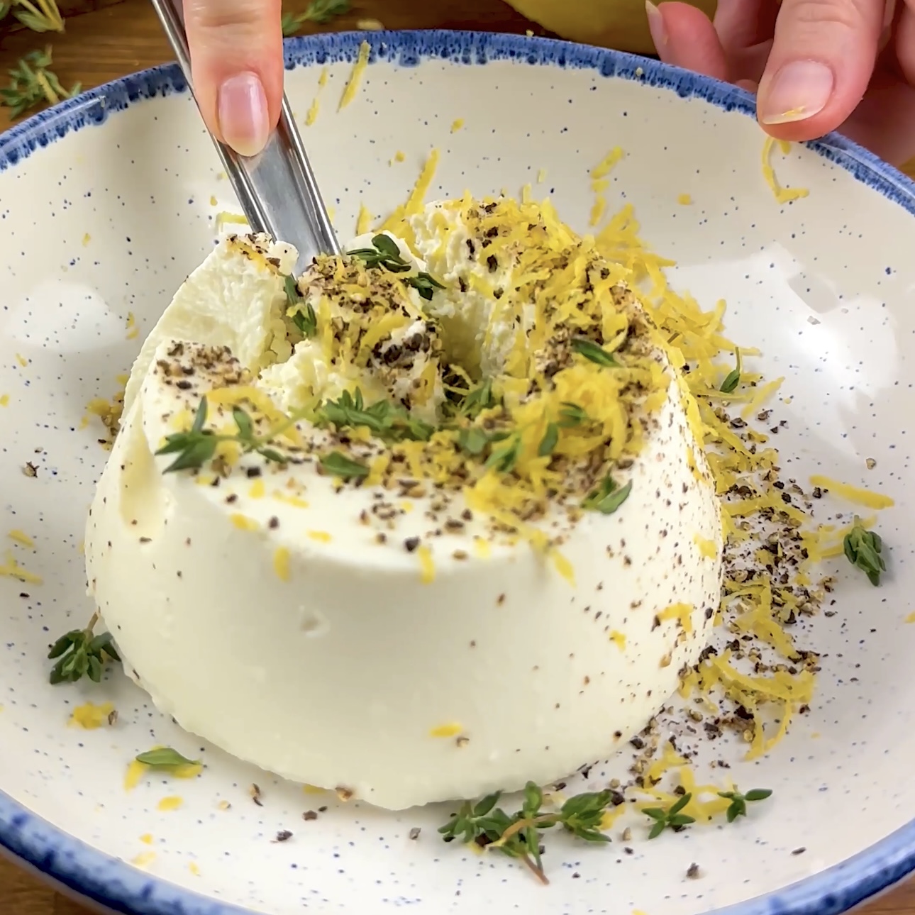 A photo of ricotta cheese mixed with thyme leaves, lemon zest, salt, and pepper in a bowl.