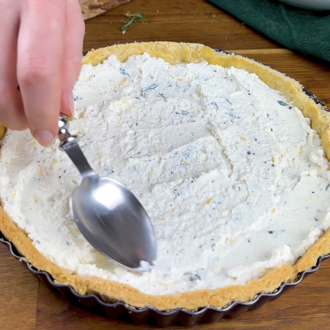 A photo of ricotta mixture being spread evenly over the base of a tart case