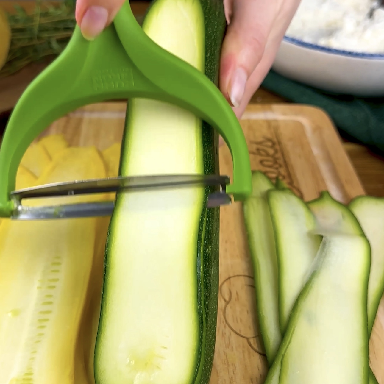 A photo of courgette being sliced into thin strips using a vegetable peeler.