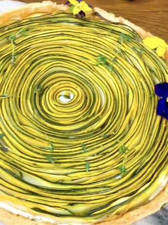 A photo of a freshly baked courgette ricotta tart, showing a golden crust with neatly arranged courgette slices on top.