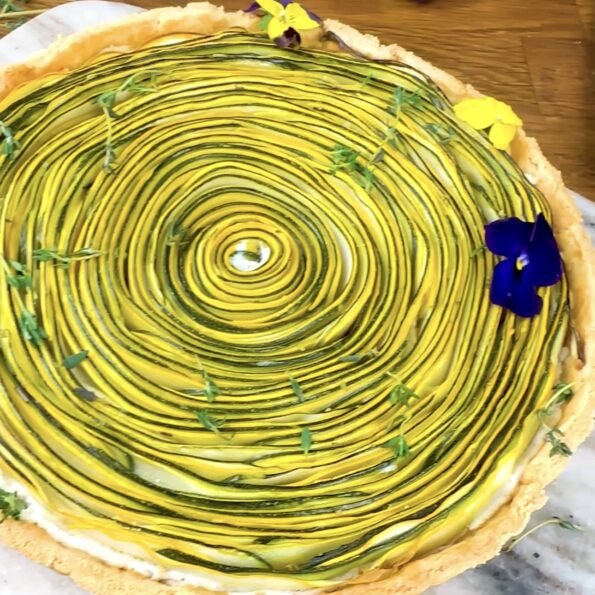 A photo of a freshly baked courgette ricotta tart, showing a golden crust with neatly arranged courgette slices on top.