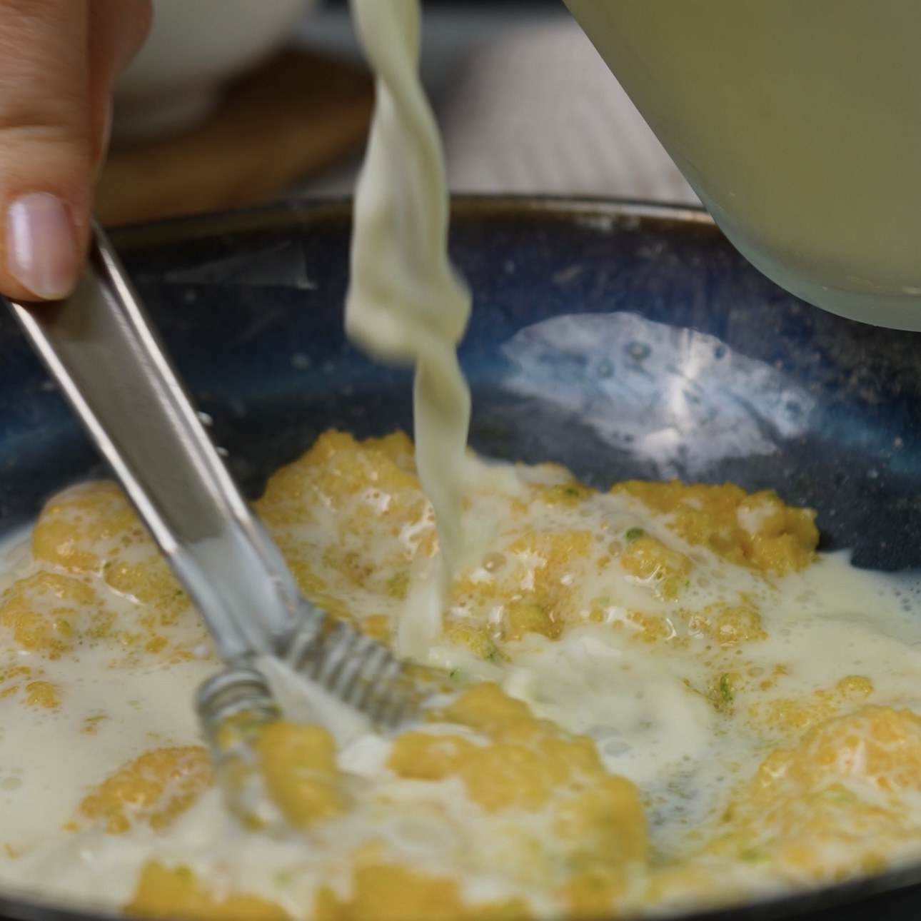 Milk being poured into a bowl with an egg yolk mixture.