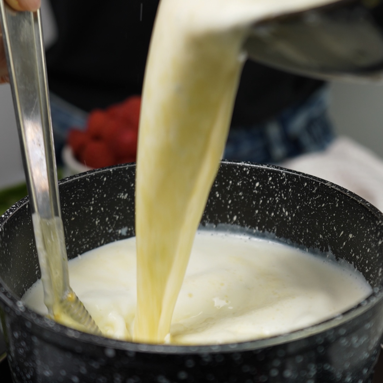 Egg yolk mixture being poured into a pot of hot milk, preparing the custard for the Creamy Raspberry Bites