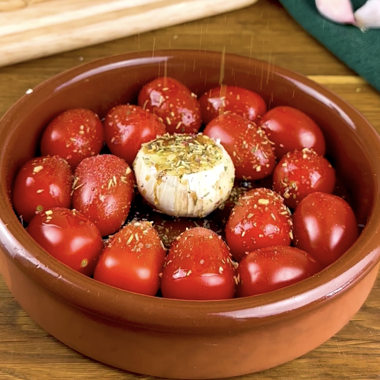 Cherry tomatoes and a bulb of garlic drizzled with olive oil and balsamic vinegar, ready to be roasted in a baking dish.