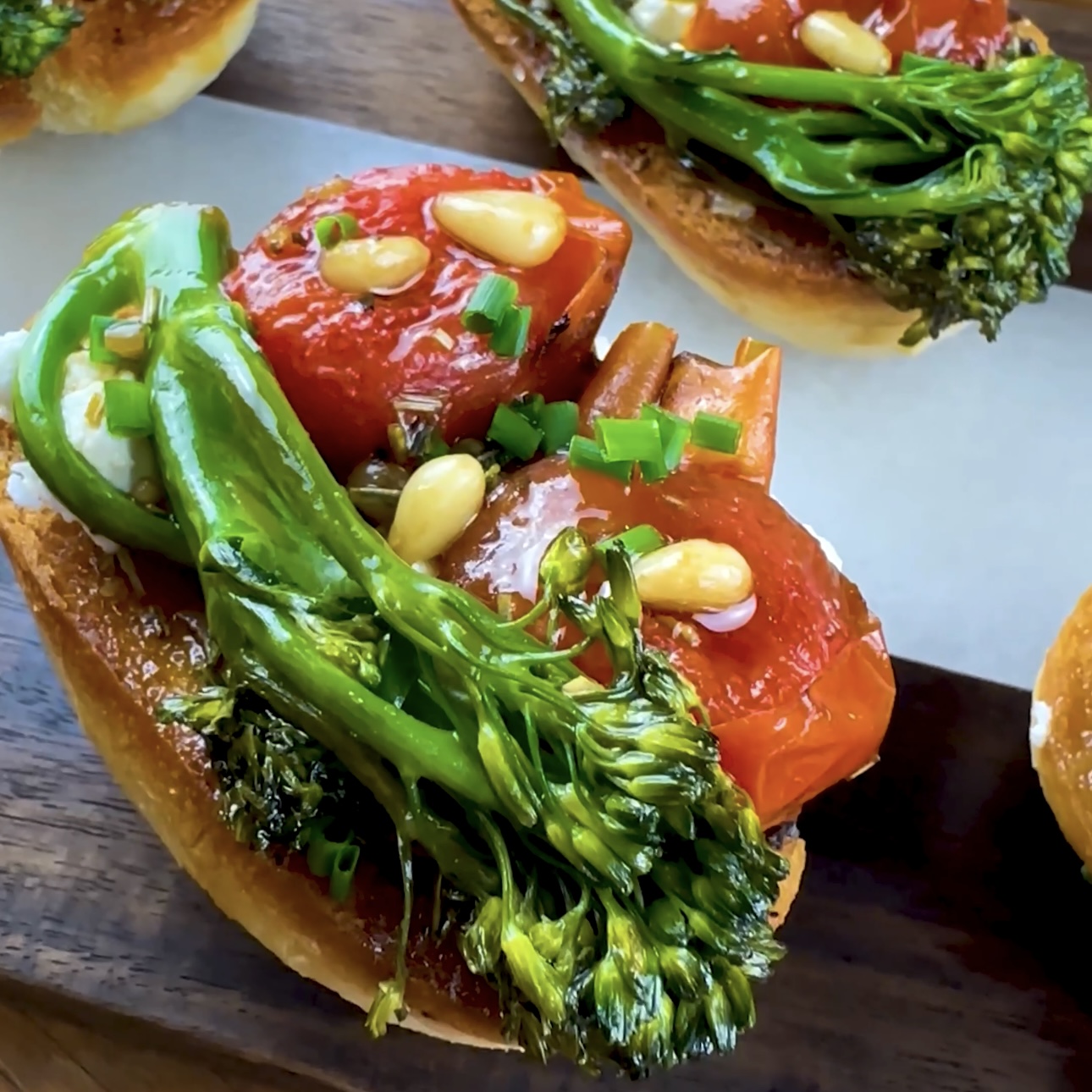 Roasted tomato goat cheese toast topped with fresh herbs on a wooden board