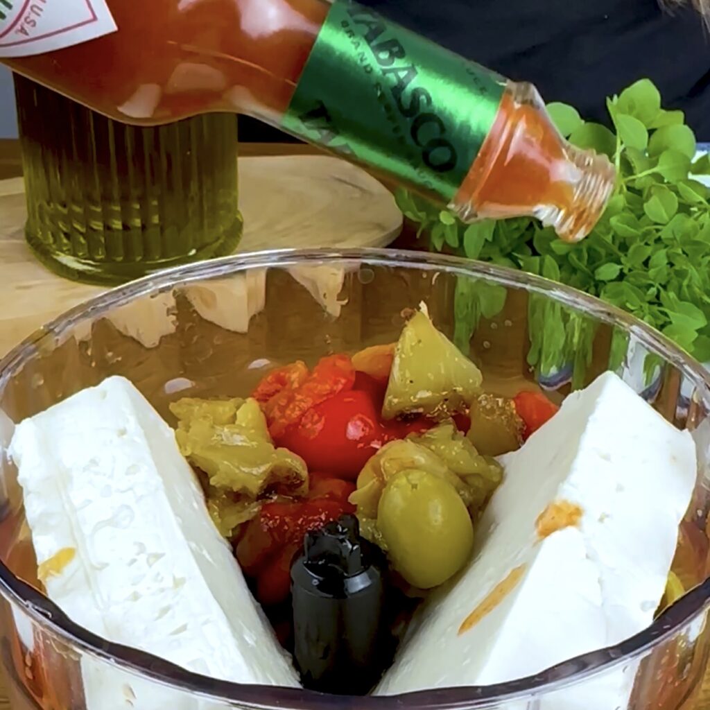 Tabasco sauce is added to a blender filled with ingredients