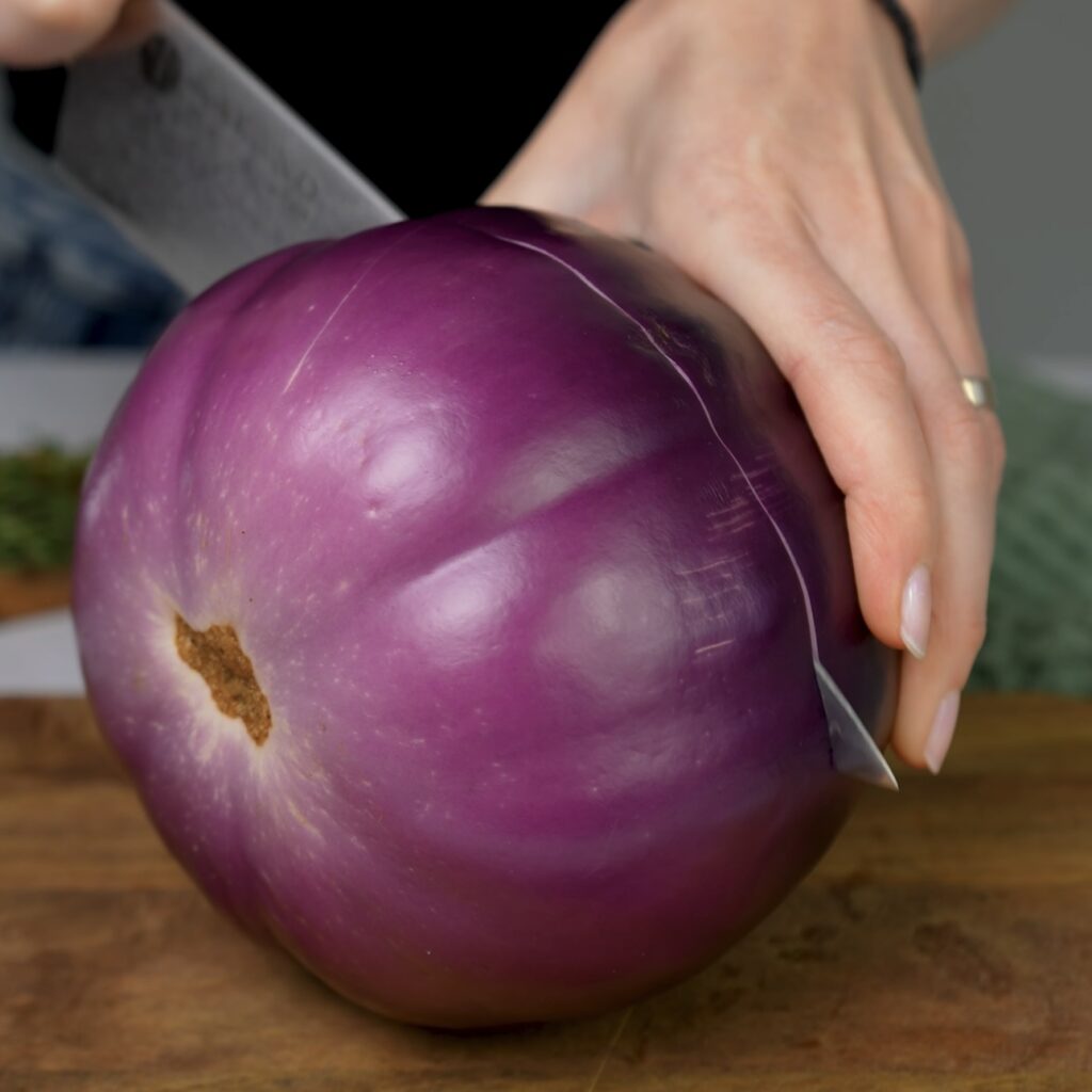 Cutting a round aubergine on a cutting board with a knife.