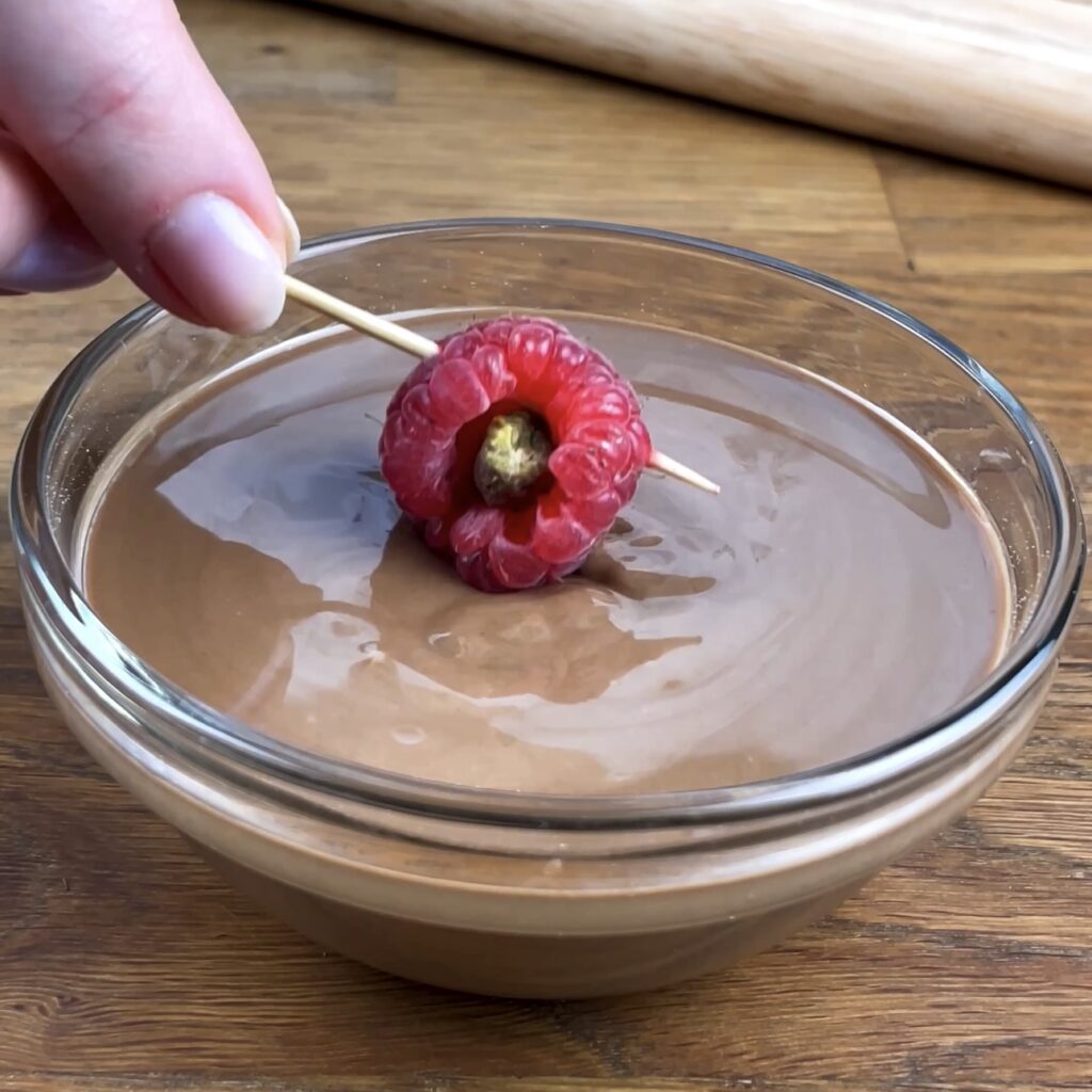 Piastachio-Stuffed Raspberry on a toothpick being dipped into melted chocolate