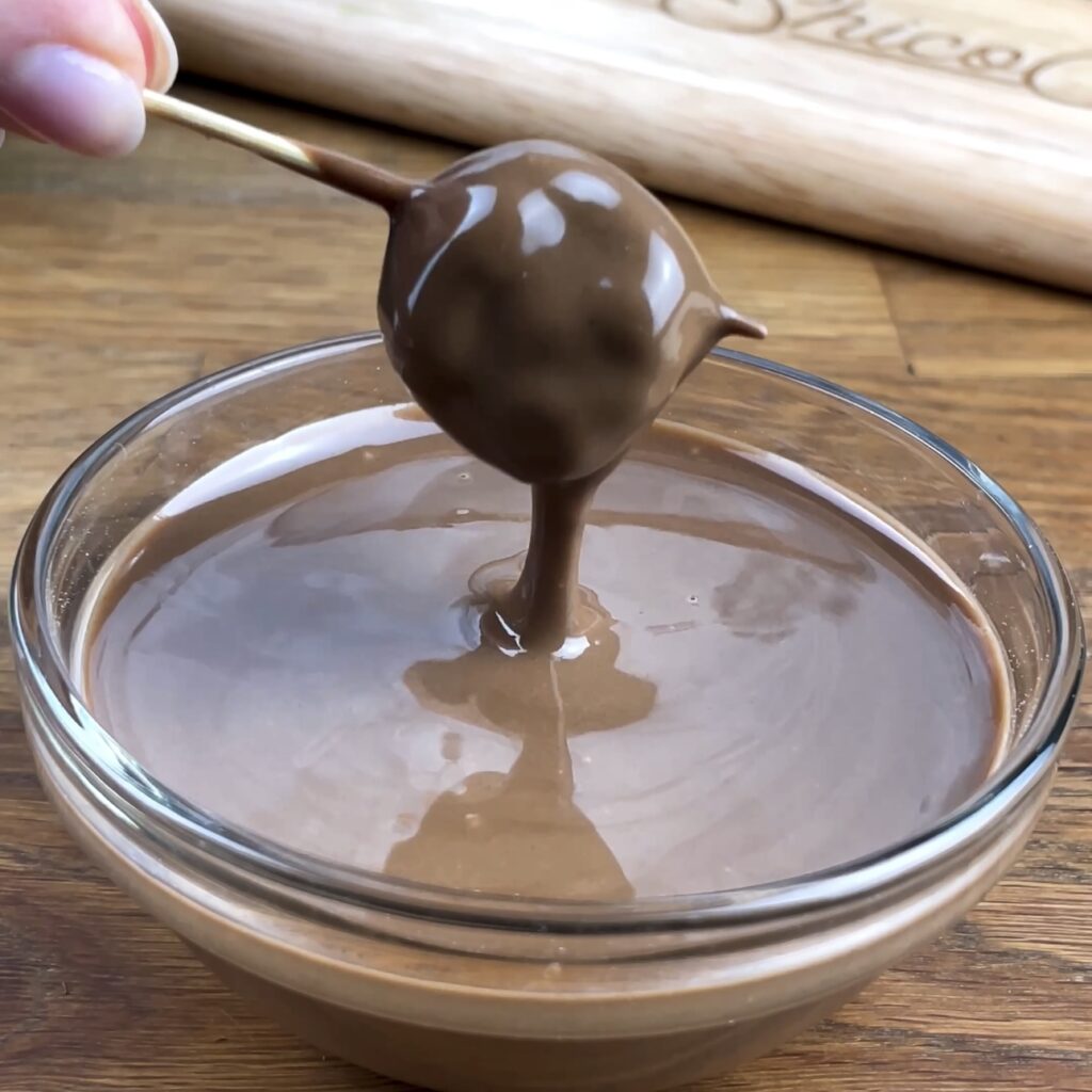 Pistachio-stuffed raspberry being dipped into melted milk chocolate.