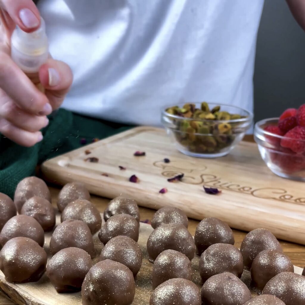 Pistachio-stuffed raspberries being sprinkled with edible gold glitter.