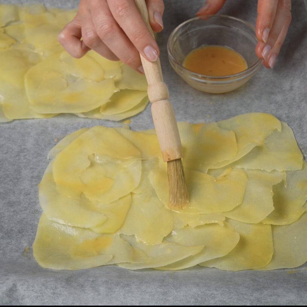 Brushing potato slices with egg wash before baking.