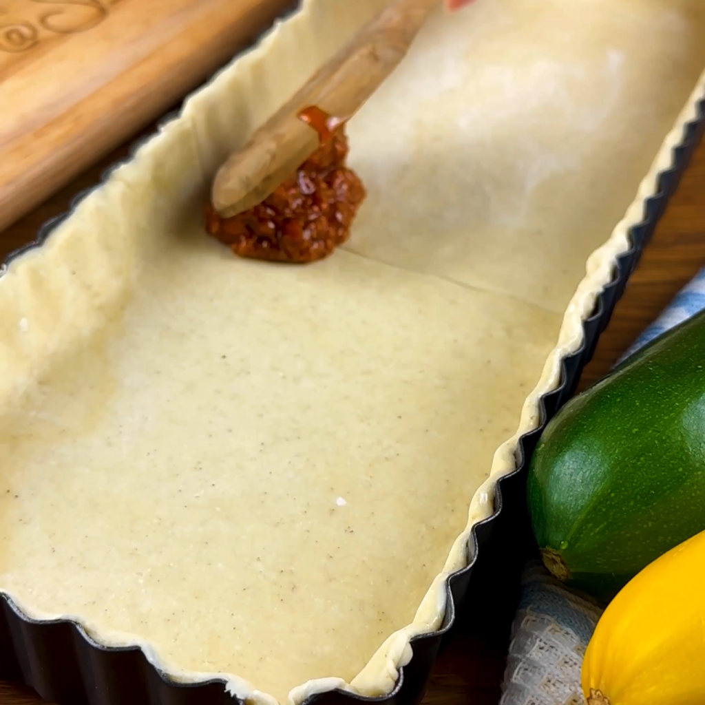 Sundried tomato pesto being spread on a tart base.