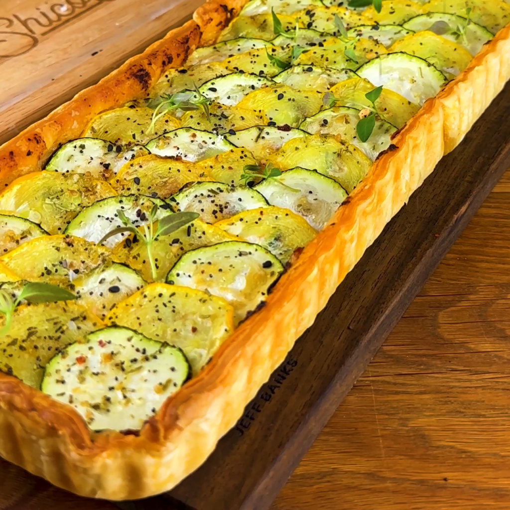 A courgette sun-dried tomato pesto tart topped with sliced courgettes and fresh herbs.