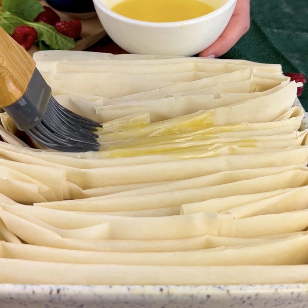 Filo pastry sheets brushed with melted butter in a baking dish.