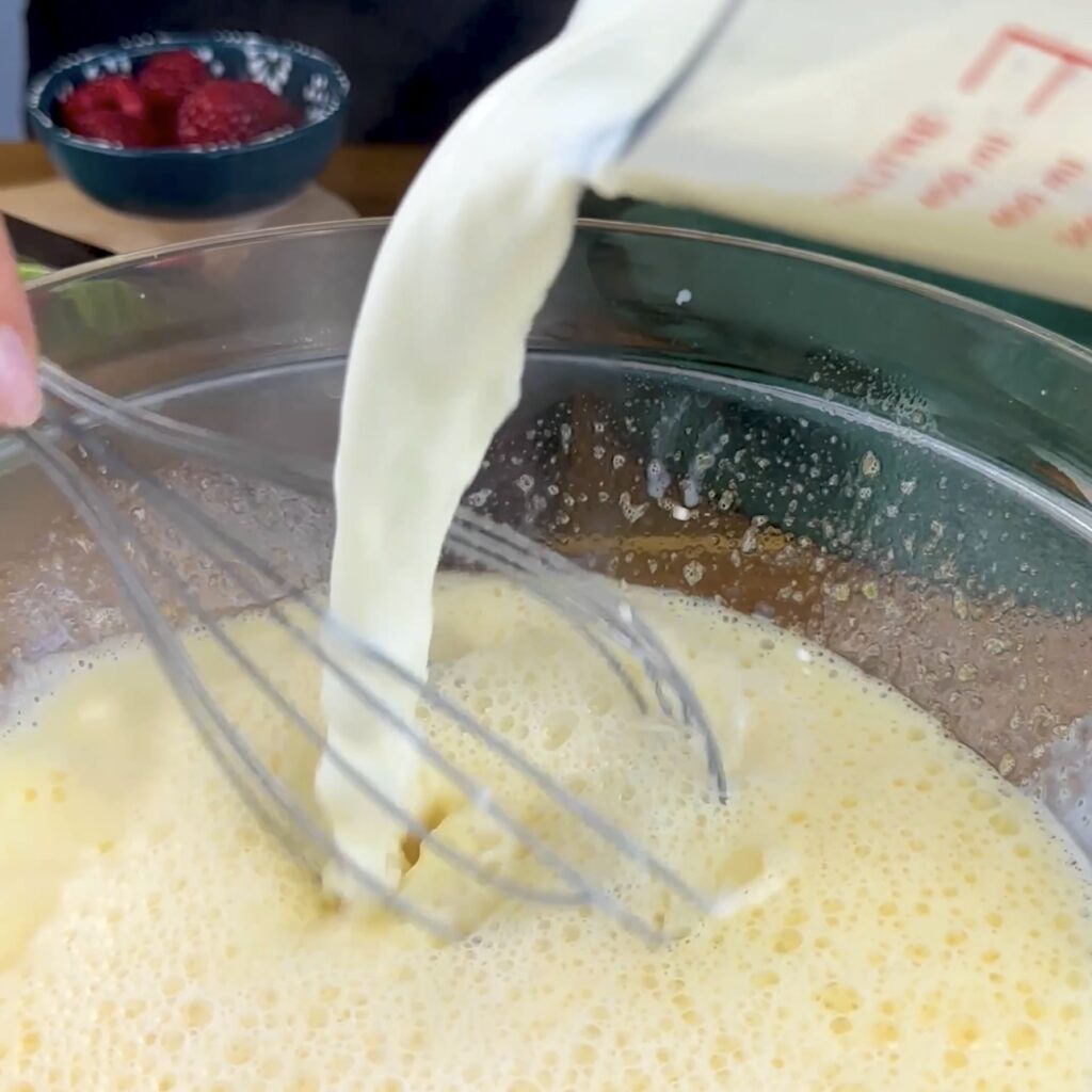 Hot milk being poured into an egg mixture in a bowl.