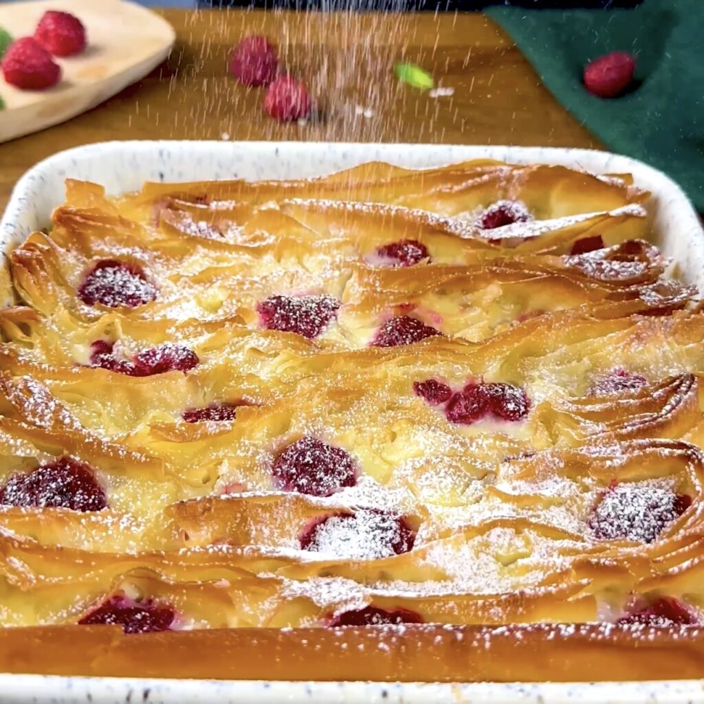 Icing sugar being dusted on top of a baked Raspberry Ruffled Milk Pie.