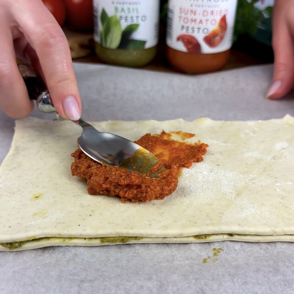 Spreading sun-dried tomato pesto evenly on a section of puff pastry.