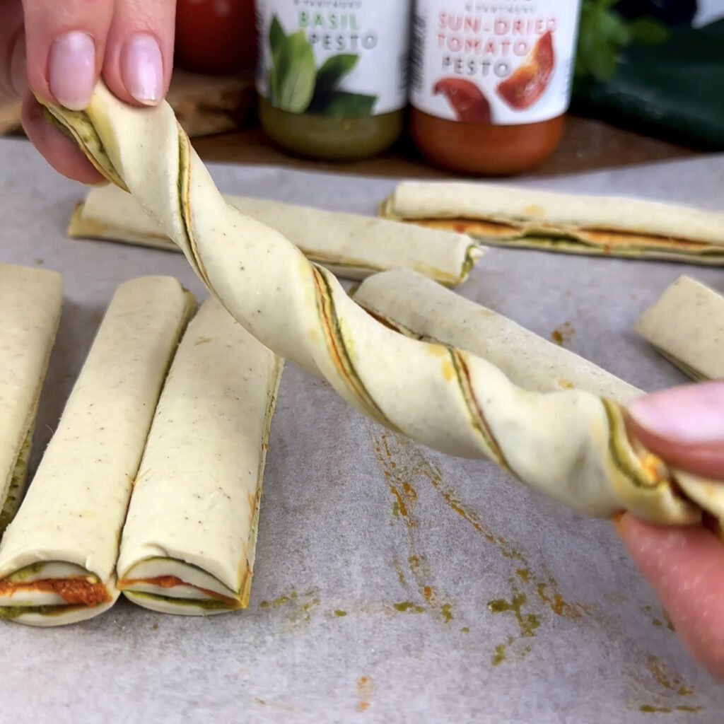 Twisting strips of puff pastry to form Pesto Twists.