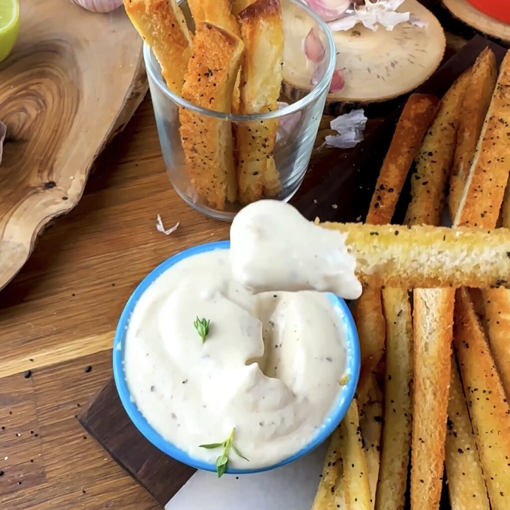 A breadstick being dipped into creamy roasted garlic dip.