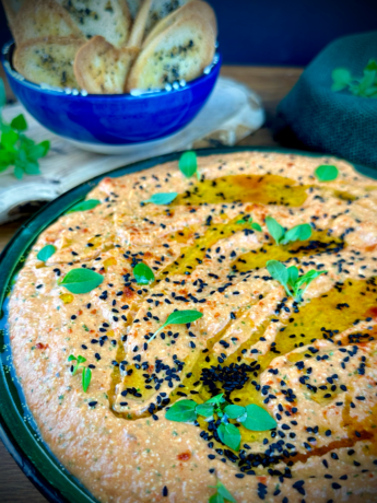 A bowl of creamy Roasted Red Pepper and Feta Dip garnished with nigella seeds and fresh basil leaves.