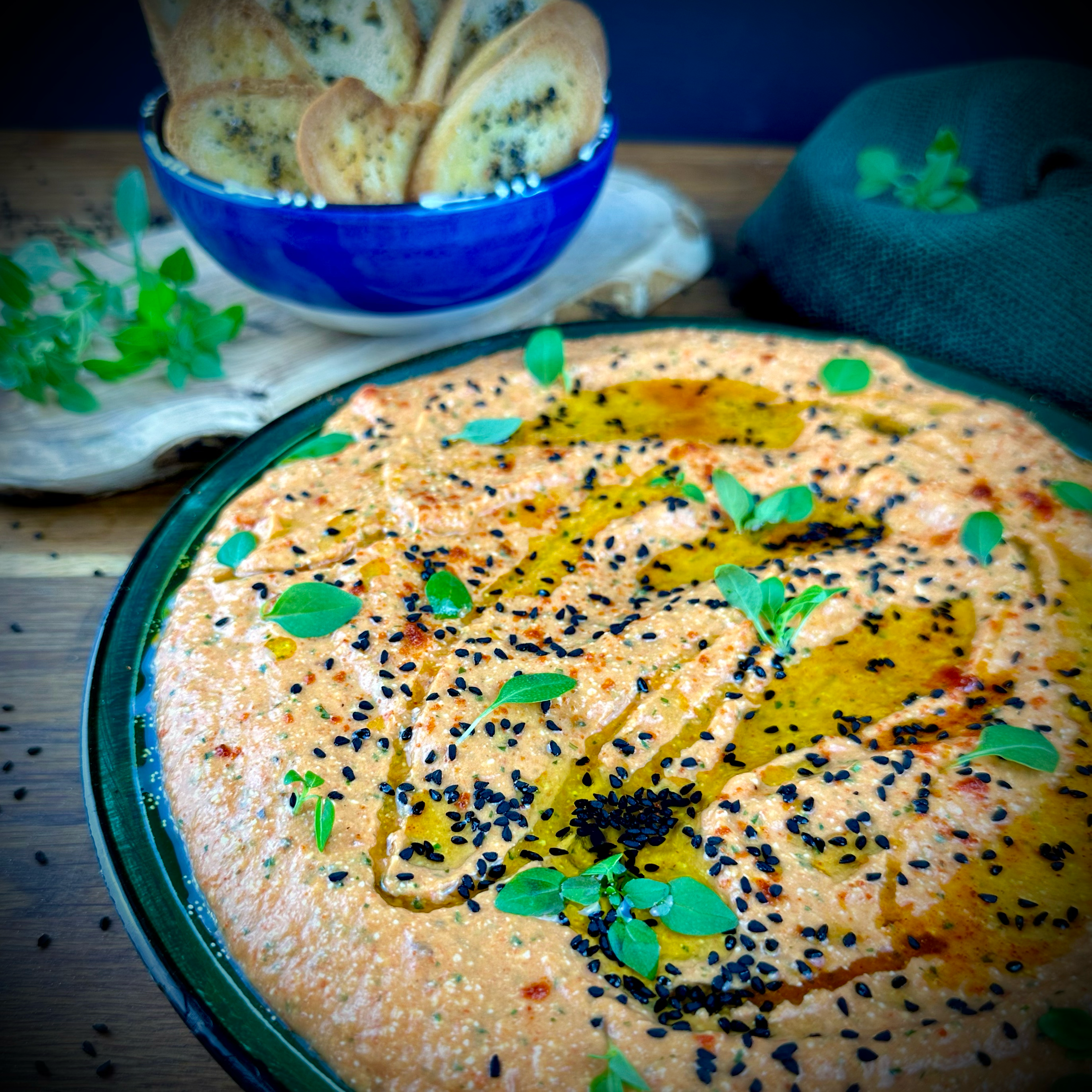 A bowl of creamy Roasted Red Pepper and Feta Dip garnished with nigella seeds and fresh basil leaves.